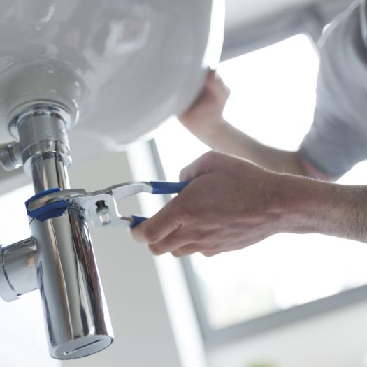 Idraulico professionista che ripara un lavandino del bagno che perde, utilizzando le pinze della pompa dell'acqua.