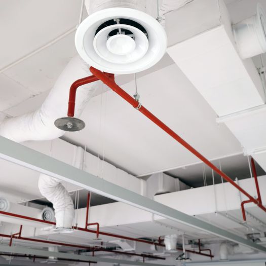 Vista prospettica del condotto dell'aria bianco sul soffitto con il tubo rosso dello sprinkler dell'acqua.